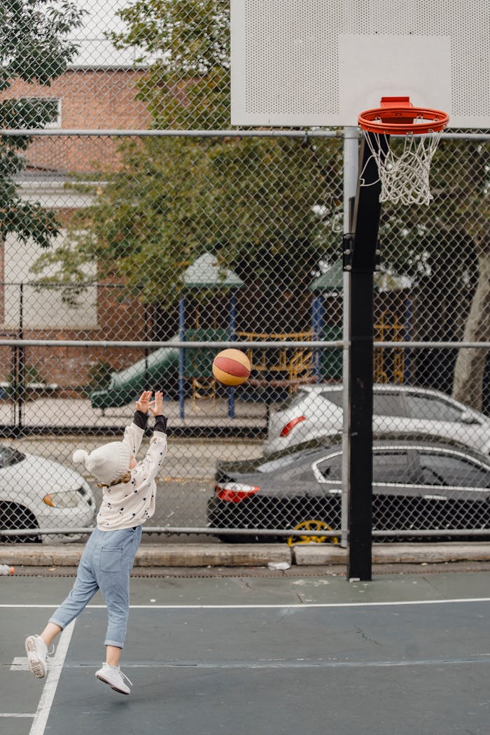 Side view full body of unrecognizable little kid throwing ball into hoop while playing game on sports ground on street